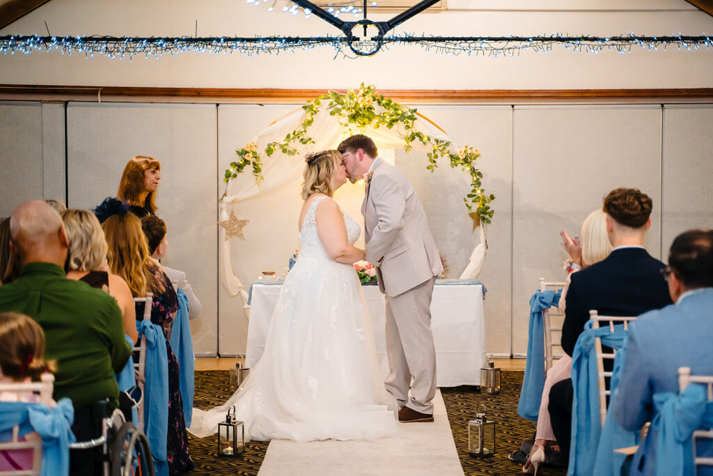 Kay and Steven's first kiss under a floral arch in the Horseshoe Barn at the Stables Country Club