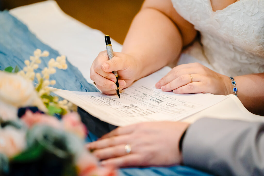Close-up of Kay signing the wedding register with blue and pink flowers beside her