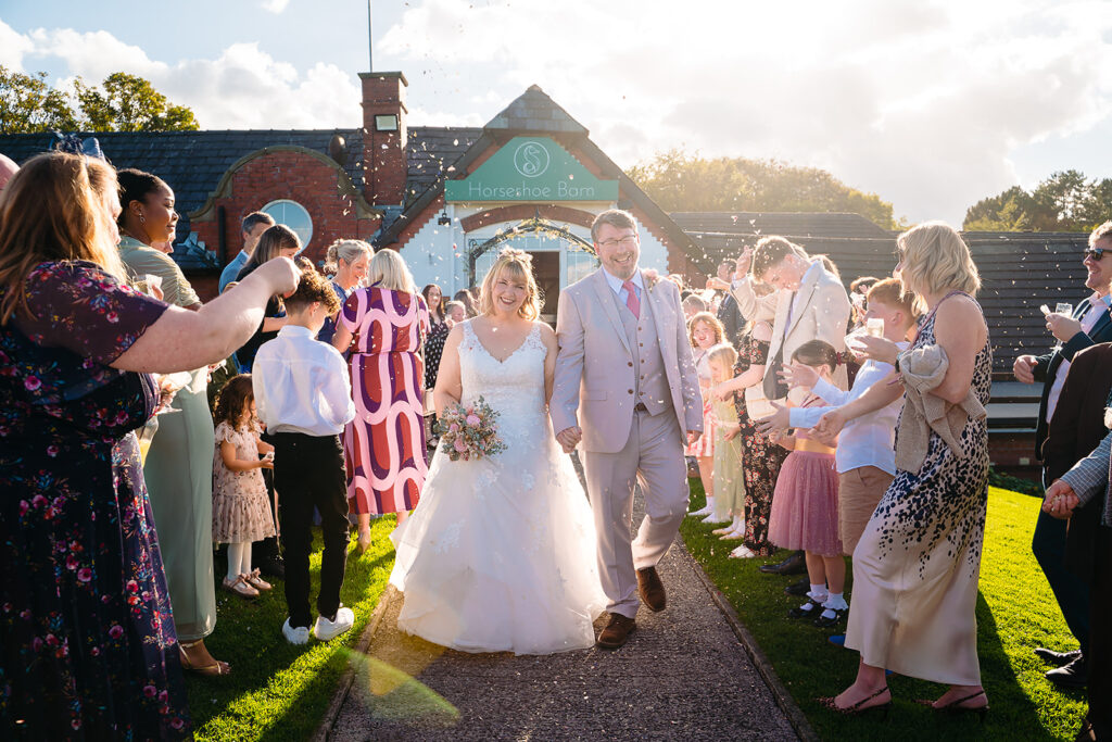 Kay and Steven walking down the path from the Horseshoe Barn through confetti from both sides