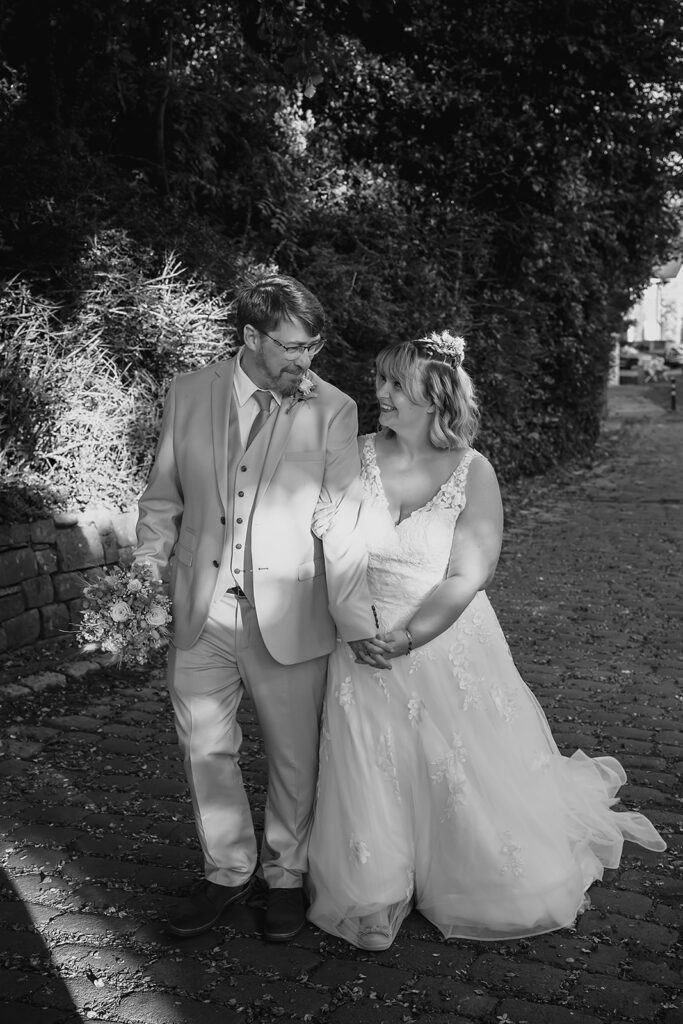 Black and white photo of Kay and Steven walking arm in arm along a woodland path