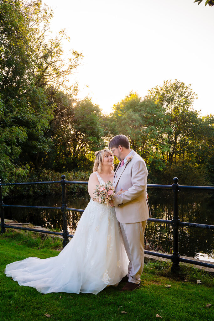 Kay and Steven by the railings at the lake's edge as the sun sets behind the trees