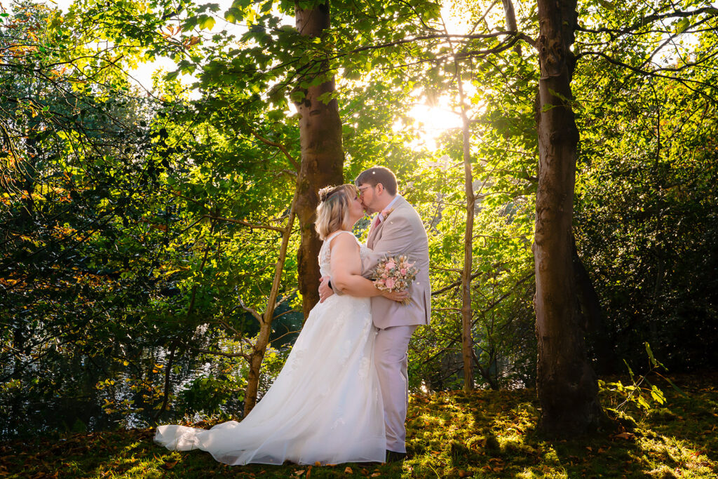 Kay and Steven kissing between two tall trees in golden evening light