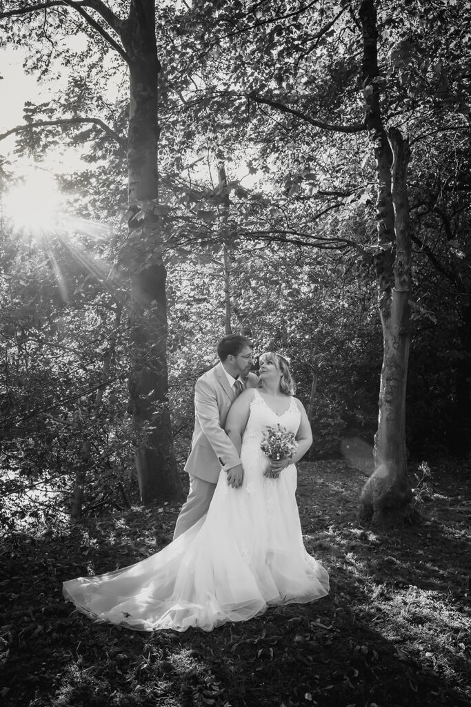 Black and white photo of Kay and Steven by the water's edge, with her dress spread across the grass