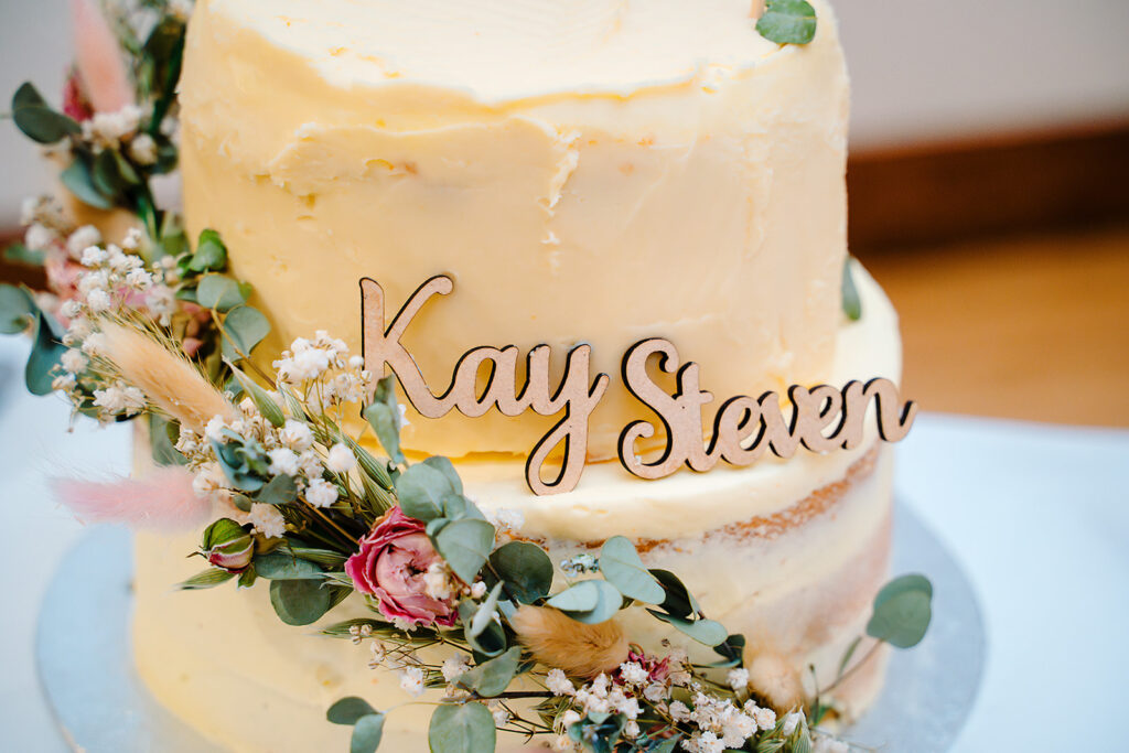 Wooden Kay and Steven topper on a semi-naked wedding cake decorated with dried flowers