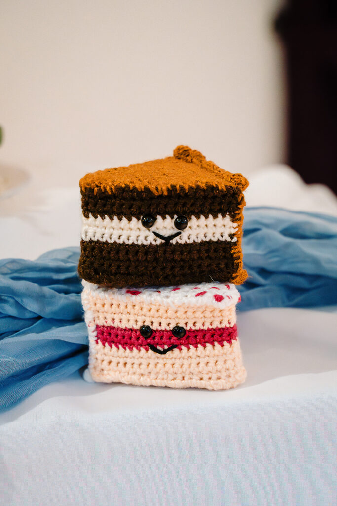 Two crocheted cake slices with smiling faces on the wedding cake table