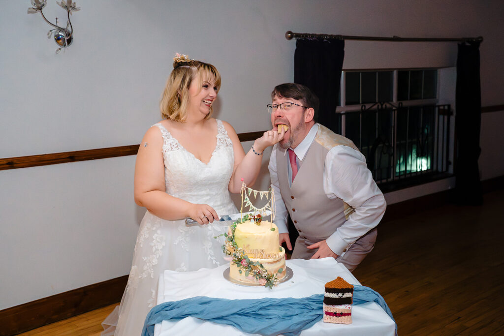 Kay laughing as Steven licks icing from his finger while they cut their wedding cake