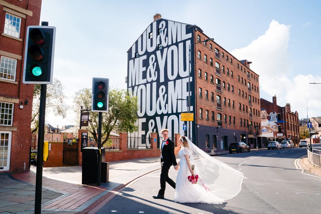 Bride and groom crossing street near mural, Leeds.