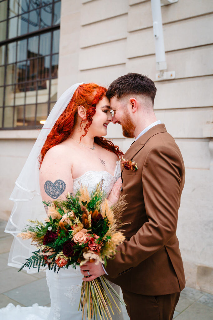 Bride and groom embracing with bouquet outside Leeds Civic Hall.