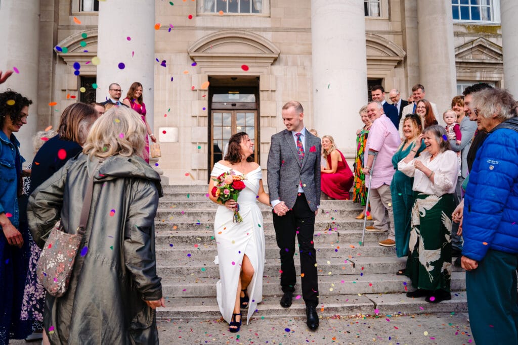 Wedding couple exits, guests throw confetti.