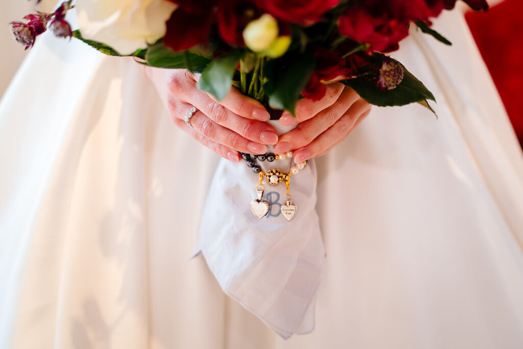 Rebecca holding her bouquet of deep red roses, wrapped in an embroidered handkerchief with heart charms