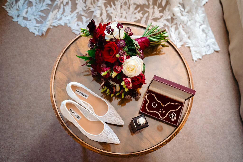 Lace Steve Madden heels, a pearl necklace and a red and white rose bouquet on a round table at Holdsworth House