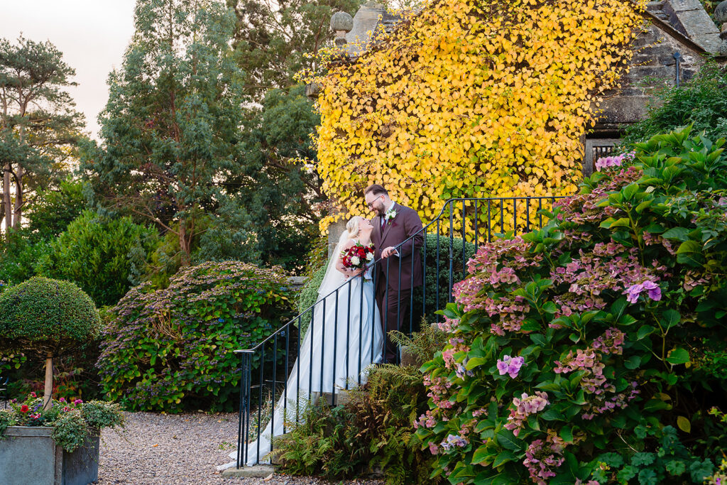 Rebecca and Nicholas kissing on stone steps under golden autumn ivy at Holdsworth House