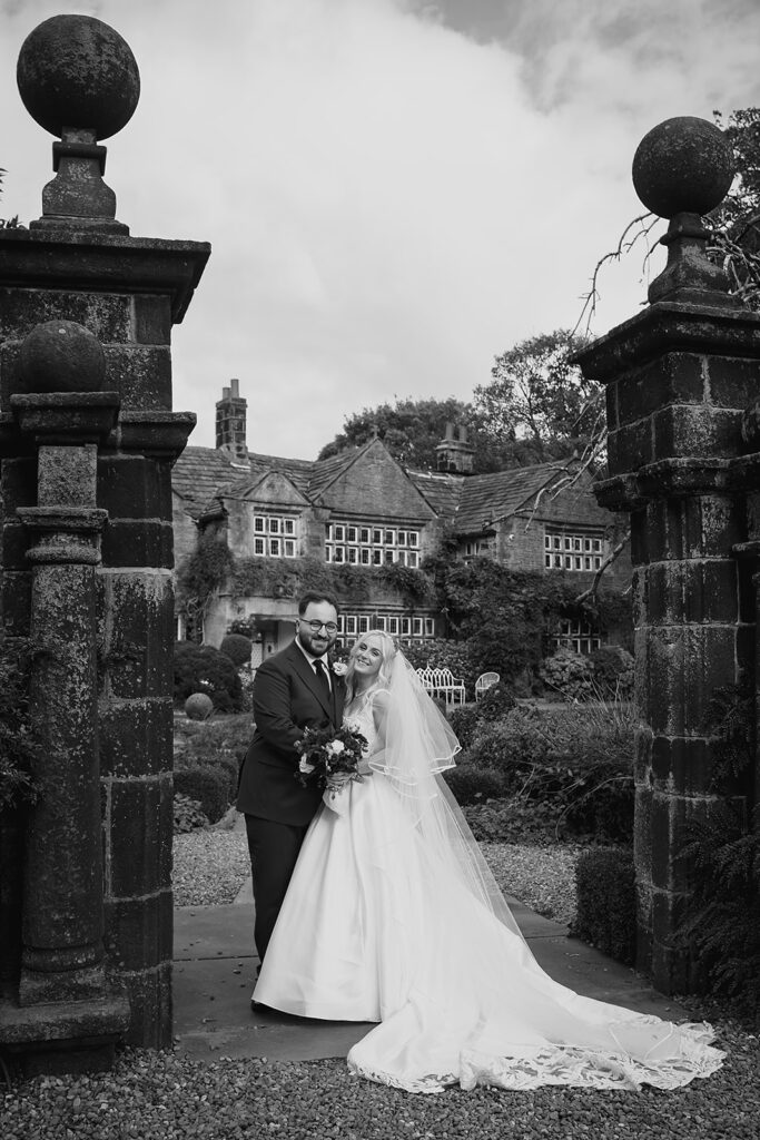 Black and white photo of Rebecca and Nicholas between the old stone gate pillars at Holdsworth House