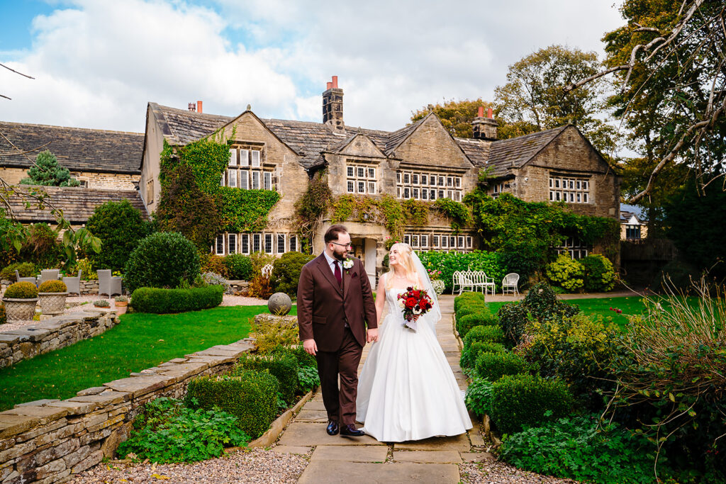 Rebecca and Nicholas walking hand in hand through the gardens in front of Holdsworth House