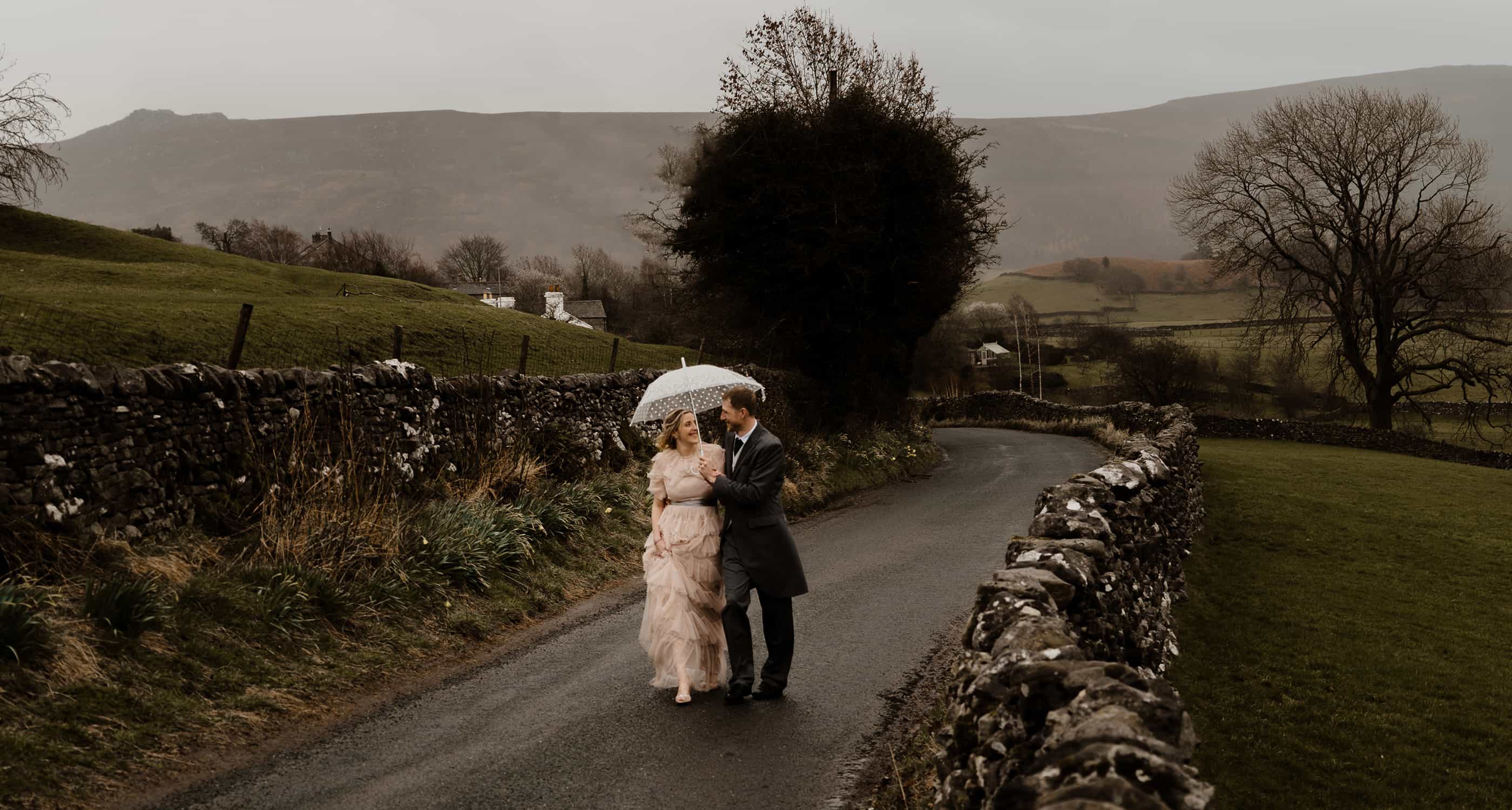 Groom and Bride walk in Yorkshire Dales under umbrella