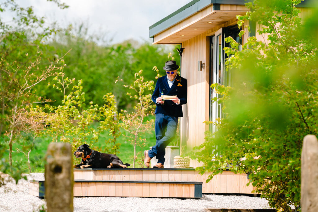 Man reading by house, dog lying nearby outside before wedding at The Out Barn