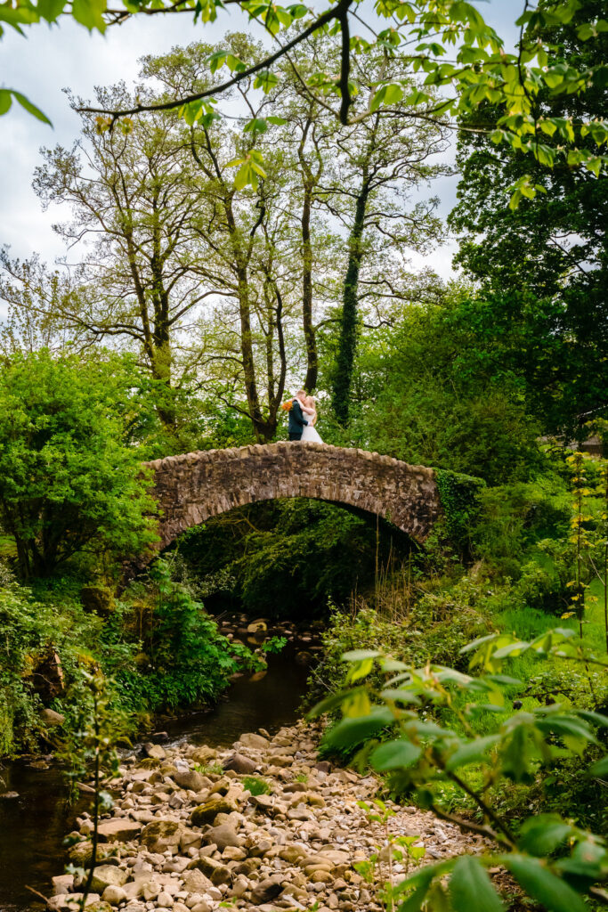 Couple embracing on stone bridge over scenic stream.