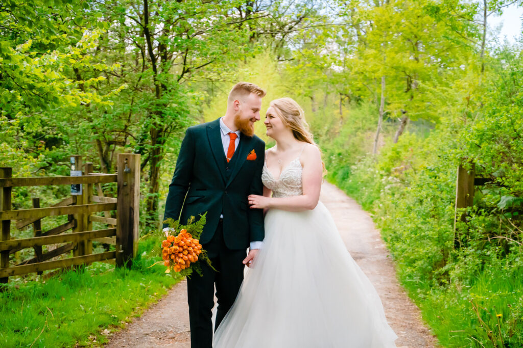Bride and groom walking in a green woodland path walking towards The Out Barn.