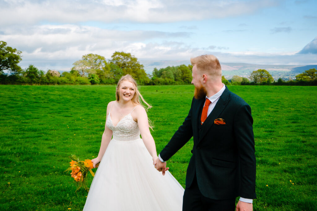 Couple holding hands in green field near The Out Barn