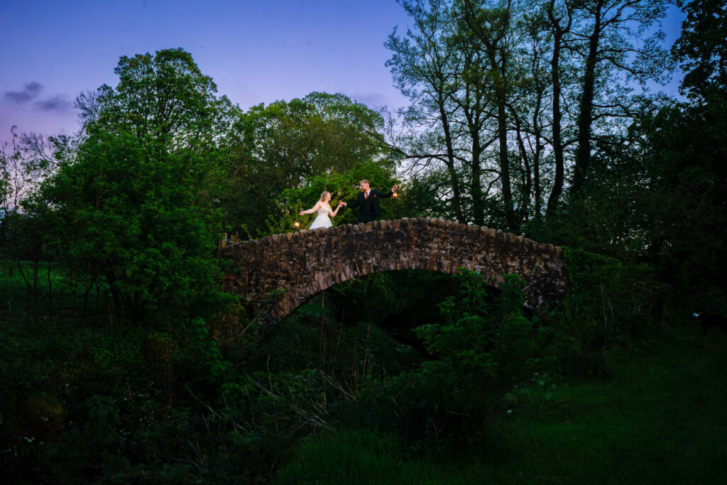Couple on stone bridge in lush evening setting near The Out Barn.