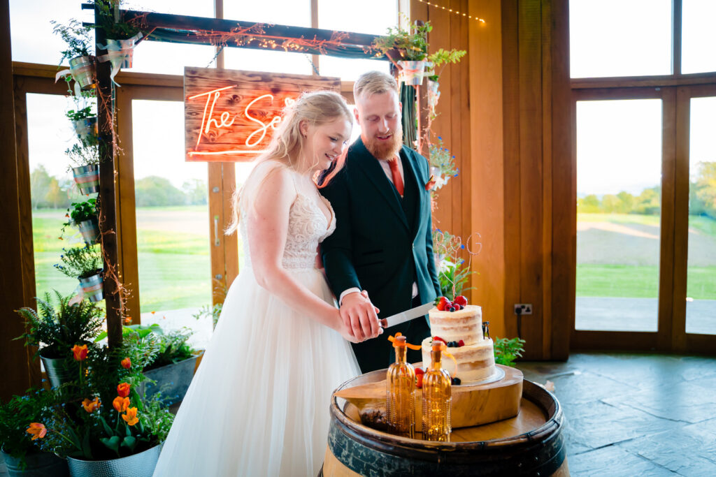 Couple cutting wedding cake at reception at The Out Barn