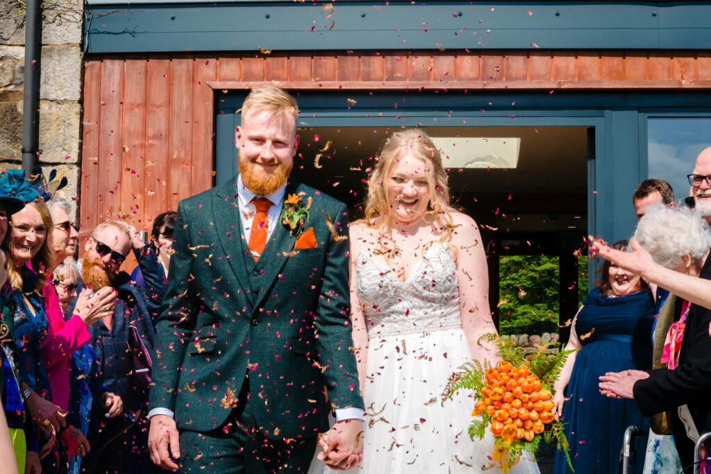 Joyful wedding couple exits The Out Barn under confetti shower.