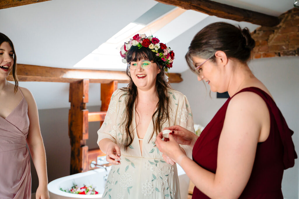 Bridesmaids laughing as they help the bride into her dress before the Priests House wedding
